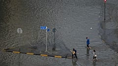 Pendler waten nach heftigen Regenfällen durch eine überflutete Straße in Schardscha in den Vereinigten Arabischen Emiraten am Mittwoch, dem 25. März 2026.
