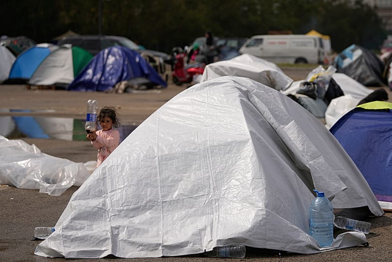 Une jeune fille près de tentes recouvertes de bâches en plastique, dans un espace public où des personnes déplacées ont fui le Sud Liban