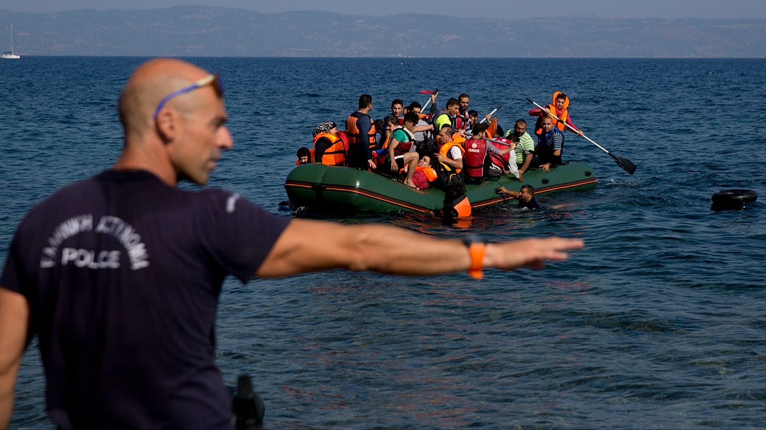 FILE: A Greek policeman gives instructions as migrants whose boat stalled at sea while crossing from Turkey to Greece approach the shore of the island of Lesbos, 20 September 