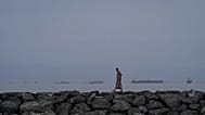 A man walks along the shore as oil tankers and cargo ships line up in the Strait of Hormuz as seen from Khor Fakkan, 11 March, 2026