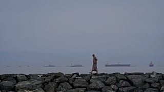 A man walks along the shore as oil tankers and cargo ships line up in the Strait of Hormuz as seen from Khor Fakkan, 11 March, 2026