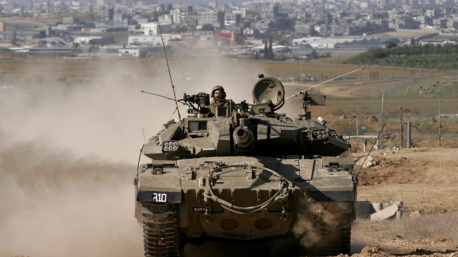 دبابة إسرائيلية تغادر قطاع غزة، في الخلفية، إلى منطقة تجمع عسكري في كيبوتس ميفالسيم في جنوب إسرائيل