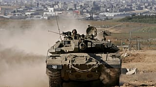 دبابة إسرائيلية تغادر قطاع غزة، في الخلفية، إلى منطقة تجمع عسكري في كيبوتس ميفالسيم في جنوب إسرائيل