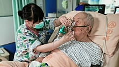Eine Pflegerin wischt einem älteren Patienten im Krankenhaus den Mund ab.