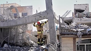 A first responder inspects the damaged structure of a residential building hit in an earlier U.S.-Israeli strike in Tehran, 27 March 2026