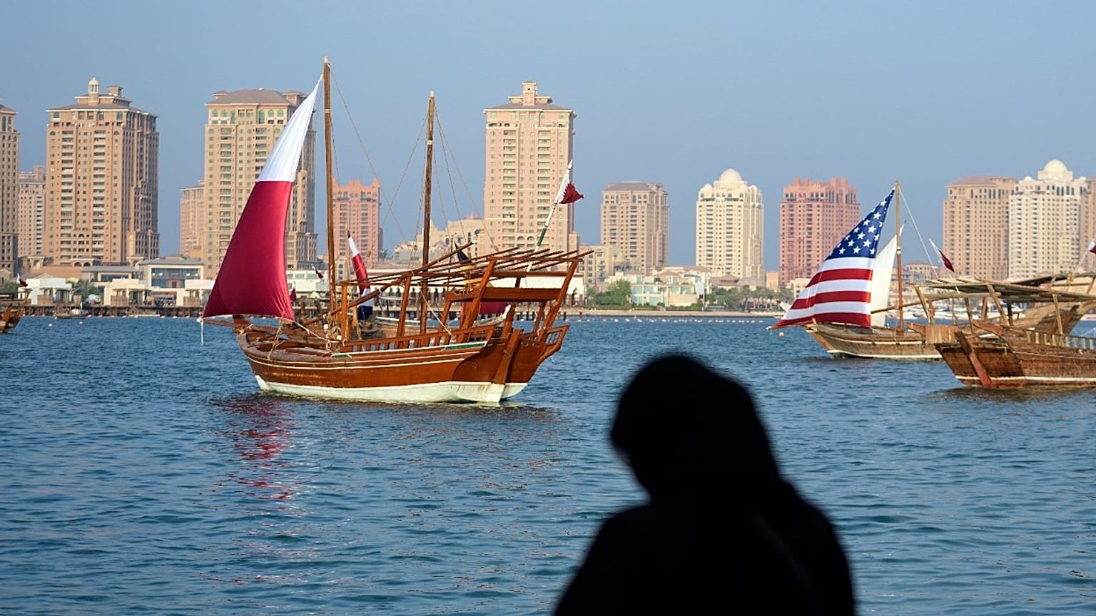 امراة تلتقط صور لقوارب شراعية بألوان علم الولايات المتحدة وقطر 