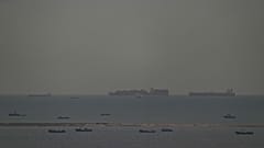 Fischerboote tummeln sich auf dem Meer, während im Hintergrund Frachtschiffe durch den Arabischen Golf in Richtung der Straße von Hormuz