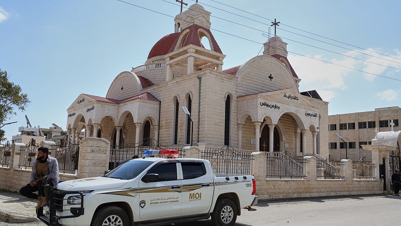 عنصر في قوى الأمن الداخلي السوري يجلس على سيارة متوقفة خارج كنيسة في بلدة السقيلبية ذات الأغلبية المسيحية، غرب حماة، سوريا، السبت 28 مارس 2026، 