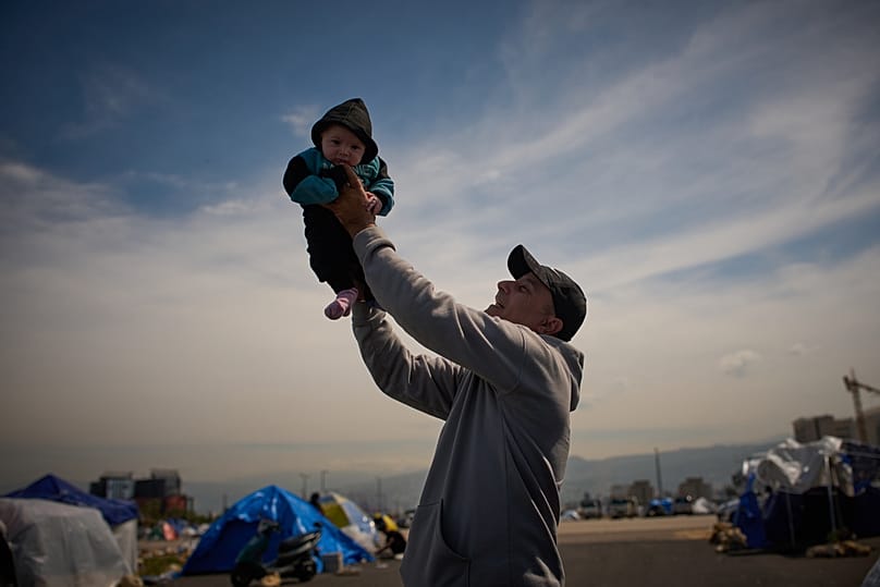 Displaced man from Beirut's southern suburbs of Dahiyeh, holds up his three-month-old son next to a tent used as a shelter in Beirut, Lebanon, Saturday, March 28, 2026