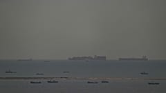 Fischerboote tummeln sich auf dem Meer, während im Hintergrund Frachtschiffe durch den Arabischen Golf in Richtung der Straße von Hormuz vor den Vereinigten Arabischen Emiraten fahren, Freitag, 27. März 2026. 