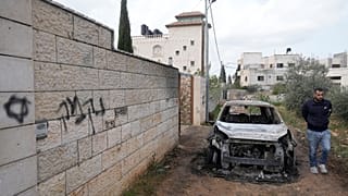 A Palestinian man inspects a torched vehicle next to Hebrew graffiti that reads "revenge", following Israeli settlers' rampage through villages in the West Bank, 23 Mar 2026.
