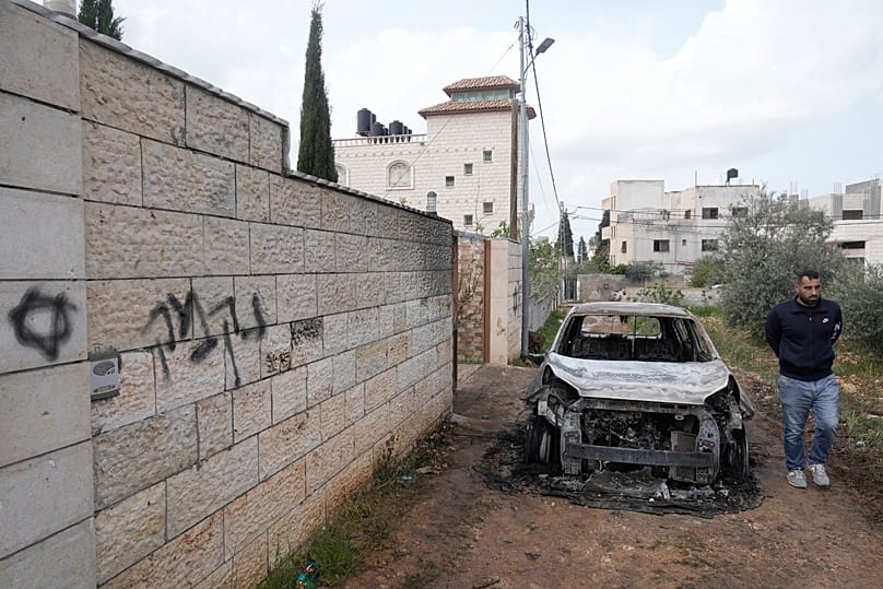 A Palestinian man inspects a torched vehicle next to a Hebrew graffiti that reads "revenge," following Israeli settlers' rampage through nearby villlages, March 23, 2026. 