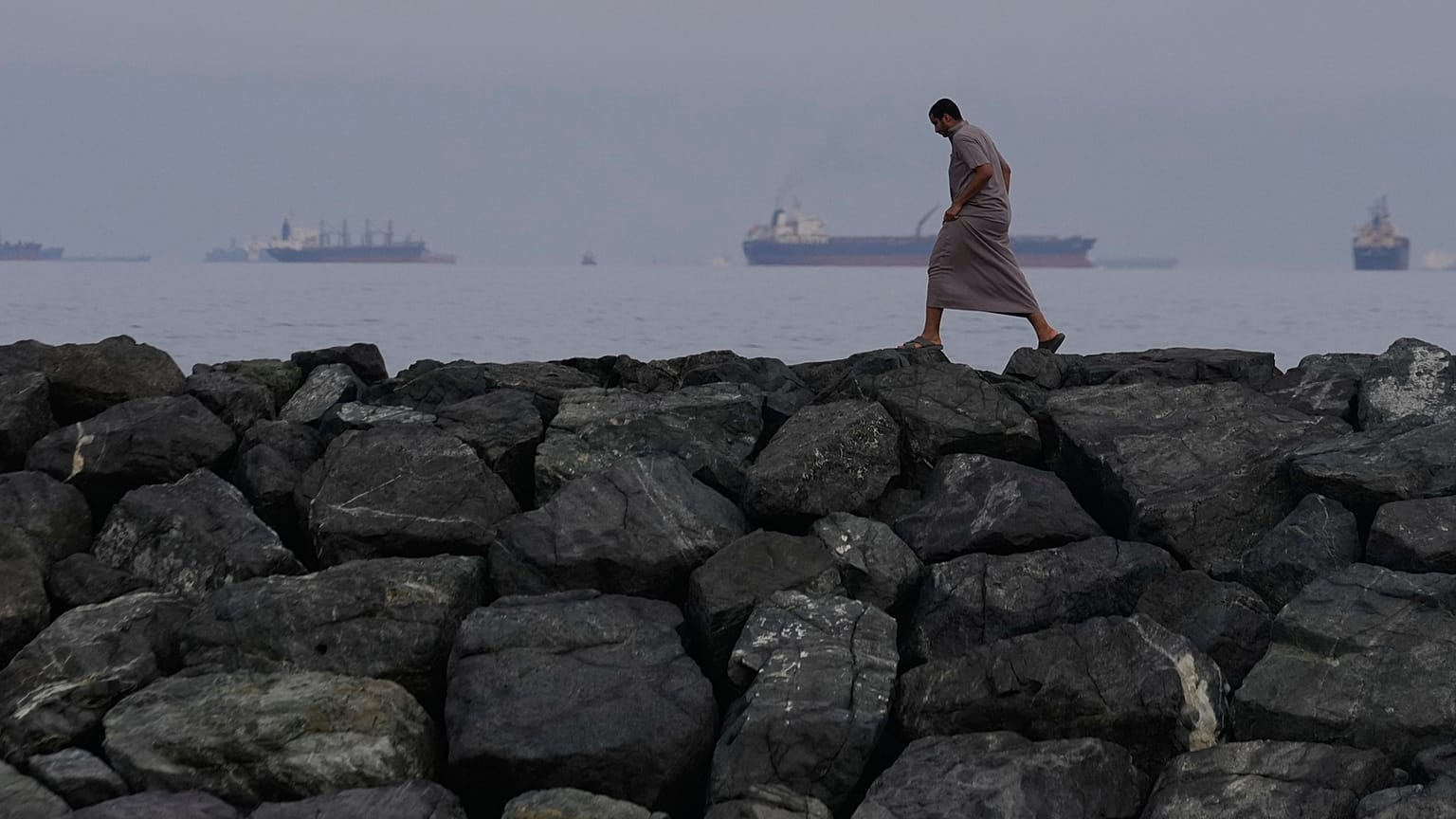 A man walks along the shore as oil tankers and cargo ships line up in the Strait of Hormuz, seen from Khor Fakkan, United Arab Emirates, Wednesday, March 11, 2026