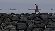 A man walks along the shore as oil tankers and cargo ships line up in the Strait of Hormuz, seen from Khor Fakkan, United Arab Emirates, Wednesday, March 11, 2026