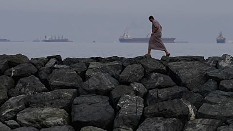 A man walks along the shore as oil tankers and cargo ships line up in the Strait of Hormuz, seen from Khor Fakkan, United Arab Emirates, Wednesday, March 11, 2026