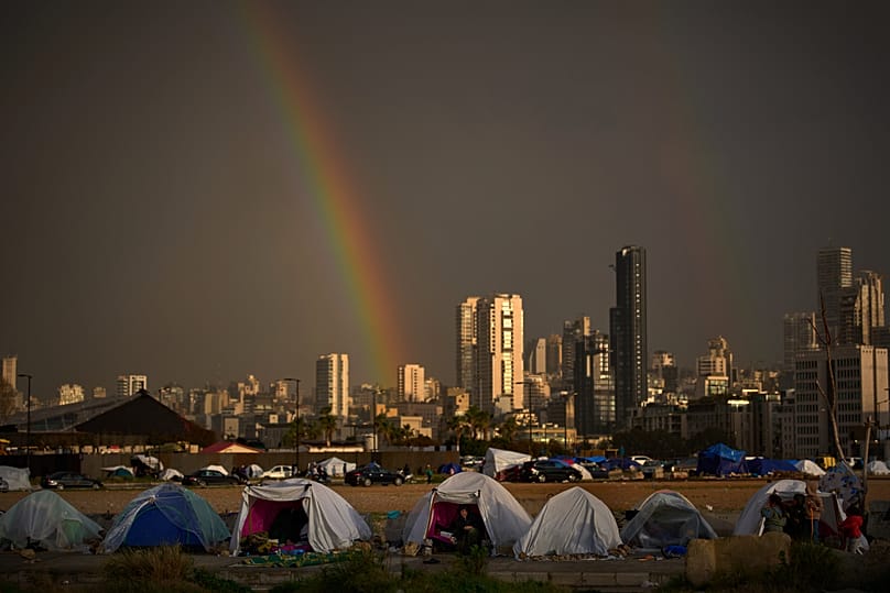 Displaced people who fled Israeli strikes in southern Lebanon sit inside tents used as shelters as a rainbow breaks through the rain in Beirut, Lebanon, Sunday, March 29, 2026