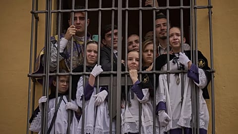 Altar boys crowd by a window to watch the Christ of the San Bernardo brotherhood pass during Holy Week in Seville on 16 April 2025.