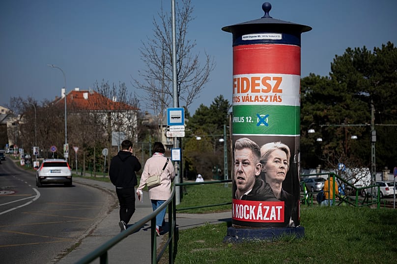 People walk next to a campaign poster which reads, "They're a risk. Fidesz is the safe choice" in Budapest, 14 March, 2026