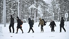 Finnische Grenzschutzbeamte begleiten Migranten, die am internationalen Grenzübergang Raja-Jooseppi zwischen Russland und Finnland eintreffen. (Symbolbild)