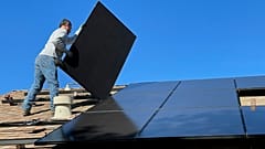 Ein Mann montiert Solarpaneele auf einem Dach.