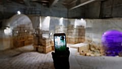 Ein Arbeiter mit einem Mobiltelefon zeigt ein Bild des Ain al-Fijeh-Stausees in Wadi Barada, Syrien, Donnerstag, 8. Mai 2025, der im Hintergrund trocken liegt.