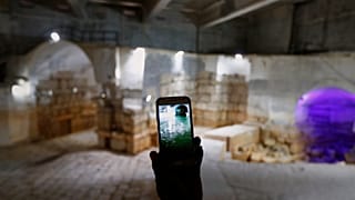 عامل يحمل هاتفاً محمولاً يعرض صورة لخزان عين الفيجة، الذي يظهر الآن جافاً في الخلفية، في وادي بردى، سوريا، الخميس 8 مايو 2025.