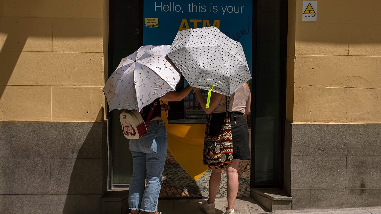 Two woman at an ATM protect themselves from the sun with umbrellas during a heatwave in Madrid, Spain, Sunday, Aug. 15, 2021. 
