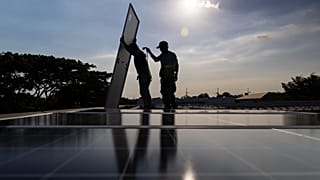 A pair of solar installers haul a solar panel onto the roof of a home in Manila, Philippines, on April 30, 2026. 
