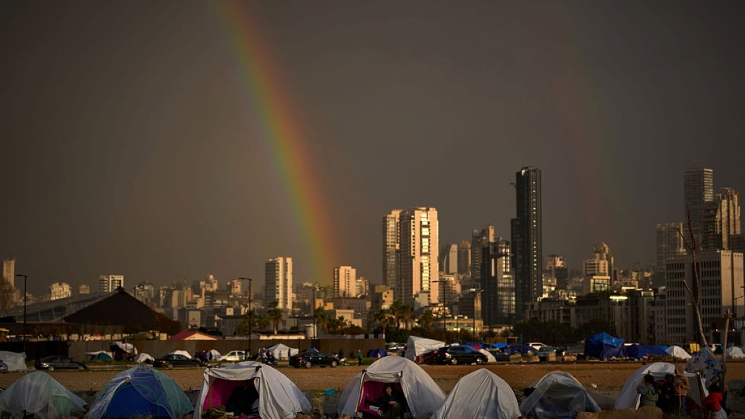  يجلس النازحون الذين فروا من الغارات الإسرائيلية في جنوب لبنان داخل خيام تستخدم كملاجئ بينما يظهر قوس قزح من خلال المطر في بيروت، لبنان، الأحد 29 مارس 2026.