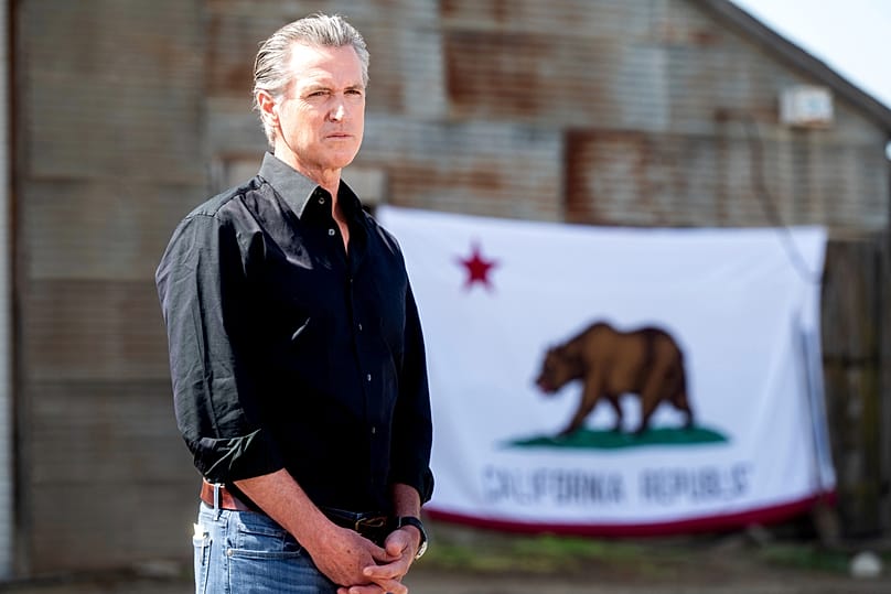 Outgoing California governor Gavin Newsom stands in front of a state flag. (AP Photo/Noah Berger)
