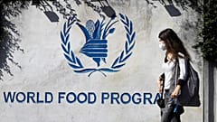 امرأة ترتدي قناع وجه تمر بجوار لافتة عند مدخل برنامج الأغذية العالمي التابع للأمم المتحدة (WFP)، في روما