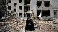 A woman sits on rubble across from a residential building damaged in air strikes in Tehran, 12 March, 2026