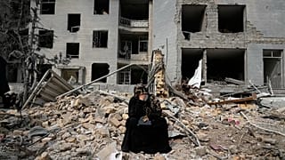 A woman sits on rubble across from a residential building damaged in air strikes in Tehran, 12 March, 2026