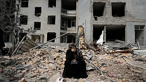 A woman sits on rubble across from a residential building damaged in air strikes in Tehran, 12 March, 2026