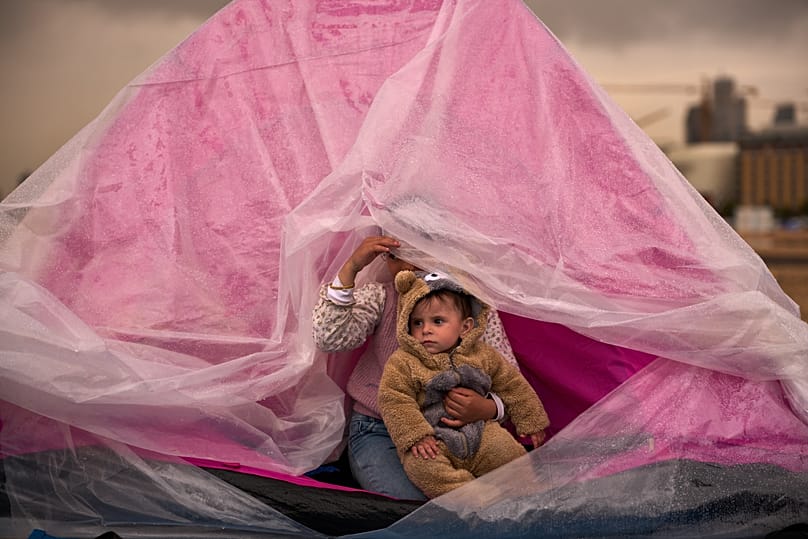 Yasmin holds her brother Ali, both displaced from Beirut's southern suburb of Dahiyeh, as they shelter from the rain inside a tent along the coast in Beirut, March 26, 2026. 