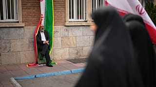رجل يتكئ على لافتة العلم الإيراني خلال احتجاج برعاية الحكومة حضره العاملون الطبيون ضد الحملة العسكرية الأمريكية الإسرائيلية خارج مستشفى الإمام الخميني في طهران