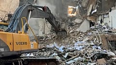 Ein Bulldozer steht vor einem zerstörten Gebäude, Rettungskräfte suchen in den Trümmern nach Überlebenden.