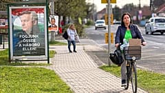 A woman rides a bicycle by a poster showing Hungarian Prime Minister Viktor Orban and the slogan "Let's stand together against the war!" in Albertirsa, Hungary, 9 April 2026