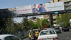 سيارات تمر أسفل لوحة إعلانية تصور المرشد الأعلى الإيراني الراحل آية الله علي خامنئي وهو يسلم العلم الإيراني لابنه مجتبى خامنئي 