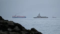 Von Khor Fakkan aus ist zu sehen, wie ein Marineschiff der Emirate neben einem Frachter durch die Straße von Hormus fährt, elf. März 2026.