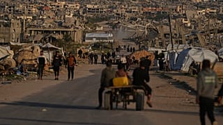 فلسطينيون يسيرون على طول شارع محاط بمبانٍ دمرتها العمليات الجوية والبرية الإسرائيلية في خان يونس، جنوب قطاع غزة، الخميس 9 أبريل 2026. (تصوير: أ.ب / عبد الكريم حنا)