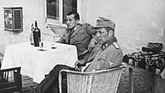 Vjekoslav Luburić, sem boné, senta-se à mesa com um oficial alemão no campo de concentração de Stara Gradiška.