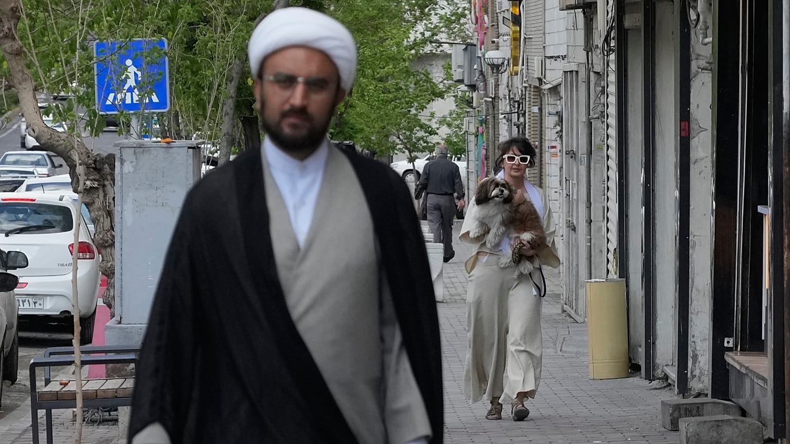امرأة تحمل كلبها بينما يسير رجل دين على أحد الأرصفة في طهران، إيران، الثلاثاء 21 أبريل/نيسان 2026. 