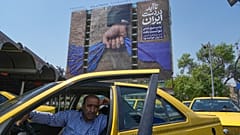 سائق ينتظر أمام لوحة بإيران تُظهر يدًا عسكرية تمسك هرمز وعبارات: "في أيدينا للأبد" و"ترامب عاجز"،  طهران، 16 أبريل 2026.