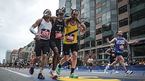 Boston Marathon runners Robson De Oliveira of Brazil, left, and Aaron Beggs, of Britain, right, helping runner Ajay Haridasse and helped him across the finish line.