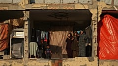Um grupo de mulheres palestinianas de pé num edifício danificado transformado em abrigo, numa área em Hamad City, Khan Younis, no sul da Faixa de Gaza, sexta-feira, 17 de outubro de 2025.