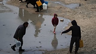 فلسطينيون يحملون عبوات بلاستيكية مملوءة بالمياه وسط طقس عاصف في مخيم للنازحين بمدينة غزة، الثلاثاء 13 يناير 2026