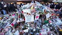  Menschen stehen um Blumen und Kerzen, die vor der abgeriegelten Bar Le Constellation in Crans-Montana, Schweiz, aufgestellt wurden, am 3. Januar 2026 (AP Photo/ Antonio Calanni)