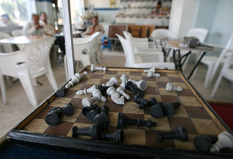 FILE: Toppled pieces are seen on a chess board as Iraqi men sit in the background at the Shako Mako Cafe, in the city of 6th October in Giza governorate, 1 September 2007