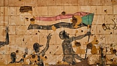لوحة تصور أشخاصاً يحملون العلم السوداني تظهر على جدار تضرر بالرصاص والشظايا في أم درمان، على مشارف الخرطوم، السودان، الخميس 23 أبريل 2026. 